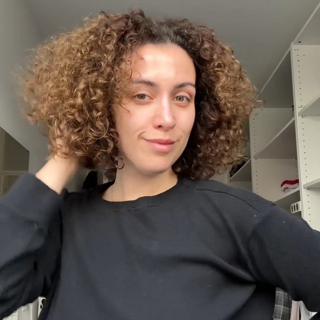 Vrouw met krullend haar poseert ontspannen in een zwarte trui in een lichte kamer met het product Unused File.