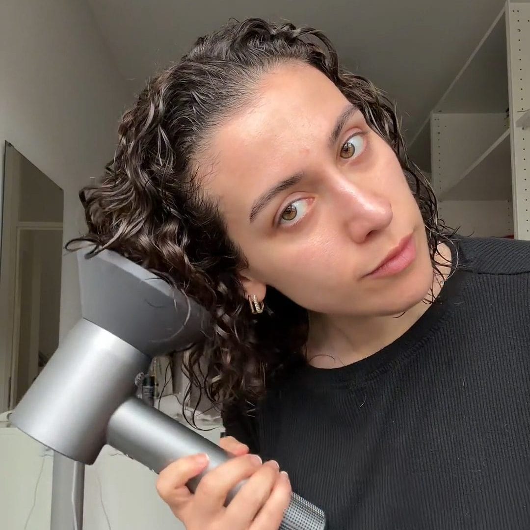 Vrouw gebruikt haardroger terwijl ze haar krullen droogt met een product genaamd Unused File.
